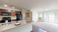 Located at 2555 Bella Colla Lane in Richland, Washington, this single-floor residence offers a thoughtfully designed open-concept layout that seamlessly connects the kitchen, dining, and living areas. The kitchen is well-appointed with rich dark wood cabinetry, black appliances including a refrigerator, range, microwave, and dishwasher, and a peninsula countertop with an integrated sink — ideal for casual dining and meal preparation. Track lighting illuminates the kitchen, while wood-style flooring runs throughout the main living areas, transitioning to plush carpet in the living room and bedrooms.

The living room is bright and welcoming, featuring a sliding glass door that opens to an outdoor balcony and allows for generous natural light. Two bedrooms provide comfortable private retreats; one includes a ceiling fan and large window with vertical blinds, while the other benefits from its own window and baseboard heating. A dedicated in-unit laundry area adds everyday convenience.

The two bathrooms are finished with dark wood vanities and wood-style flooring. One bathroom features a shower/tub combination, while the other offers a walk-in shower. Neutral tones throughout create a clean, cohesive aesthetic across the entire space.