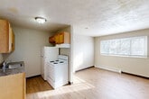 Located at 1200 Meadowview Dr in Marion, Iowa, this two-bedroom, one-bathroom unit offers a practical and efficient single-floor layout. The kitchen is equipped with warm honey-toned wood cabinetry, dark laminate countertops, a built-in sink, a white electric range with a range hood above, and a full-size refrigerator. The kitchen flows openly into the living area, which features light hardwood-style flooring and a window that allows natural light to brighten the space. Both bedrooms are carpeted and include windows fitted with blinds, offering views of the surrounding outdoor greenery. The primary bedroom provides a comfortable amount of space and includes convenient access to the full bathroom. The bathroom is outfitted with a clean, all-white tub and shower combo with a sliding glass door enclosure. Baseboard heating units are present in the living area and bedrooms, ensuring consistent warmth throughout. Neutral wall tones and textured ceilings are consistent throughout the unit, contributing to a simple, understated aesthetic. The overall layout is compact yet functional, making efficient use of every area available.