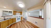 Located at 9902 Cranberry Ln NW in Silverdale, Washington, this single-floor residence offers a well-organized layout designed for comfortable everyday living. The kitchen is a functional highlight of the home, featuring warm honey-toned wood cabinetry with brushed nickel hardware, light countertops, a corner sink, a white electric range, and a dishwasher. A pass-through opening connects the kitchen to the adjacent living area, enhancing the open feel of the space. Wood-look laminate flooring flows throughout the kitchen and main living areas, adding warmth and easy maintenance.

The living room is a standout space, centered around a classic brick fireplace with a raised hearth and wood mantel. Multiple windows allow natural light to fill the room, which is finished with plush wall-to-wall carpeting. The bedroom continues the carpeted flooring and features a window with blinds overlooking greenery, along with a baseboard heater for year-round comfort.

The bathroom is clean and efficient, offering a full tub-and-shower combination with a curved curtain rod, a wood-toned vanity with a light countertop, and wood-look flooring. The textured ceilings and neutral wall tones throughout give the entire residence a bright, move-in-ready atmosphere.