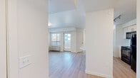 Located at 5886 Tutt Blvd in Colorado Springs, CO, this efficiently designed one-bedroom, one-bathroom unit offers a clean, modern aesthetic throughout its thoughtfully arranged floor plan. The combined kitchen and living area forms the heart of the space, featuring light wood-style flooring that extends seamlessly across the open layout. The kitchen is equipped with white cabinetry, a marble-look countertop island with a double stainless steel sink, black appliances including a range, microwave, and refrigerator, and track lighting overhead. The living area is bright and airy, with a wall-mounted HVAC unit, vertical blinds, and a glass exterior door that invites natural light and provides direct outdoor access. The bedroom offers a comfortable footprint with soft carpeting, a window with vertical blinds, and a dedicated closet for storage. The bathroom features a full tub-shower combination with a curtain rod, a toilet, and clean white walls with wood-style flooring. Throughout the unit, crisp white walls and consistent finishes create a cohesive, contemporary feel that is both functional and inviting.