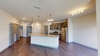 This well-appointed three-bedroom, two-bathroom residence in Sawgrass, Jacksonville, Florida, offers a thoughtfully designed single-floor layout that balances comfort and modern style. The open-concept living and kitchen area serves as the heart of the home, where rich dark wood-style flooring flows seamlessly throughout. The kitchen is a standout feature, showcasing a large granite-topped island with a built-in sink, sleek dark wood cabinetry, stainless steel appliances including a range, microwave, and refrigerator, and elegant pendant lighting that adds a contemporary touch. A dedicated pantry with open shelving provides generous storage. The living room is bright and airy, benefiting from multiple windows with horizontal blinds, a ceiling fan, and access to an outdoor space via glass doors. The primary bathroom features a dual-sink vanity with granite countertops, dark wood cabinetry, and a large mirror with modern lighting, plus a separate shower. The secondary bathroom offers a full tub-shower combination with clean white tile surround. Bedrooms are carpeted for comfort, each equipped with a ceiling fan and ample natural light from well-positioned windows, creating restful and inviting retreats throughout this move-in-ready Jacksonville residence.