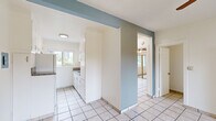 Located at 2431 S Ridgeley Dr in the West Adams neighborhood of Los Angeles, this single-floor unit offers three bedrooms, one bathroom, a living room, and a kitchen within a cozy, efficiently designed layout. Light-colored ceramic tile flooring runs consistently throughout all rooms, creating a unified and easy-to-maintain interior. The kitchen features a galley-style configuration with white cabinetry, granite-look countertops, a stainless steel sink, and a window that brings in natural light and views of surrounding greenery. Appliances including a refrigerator and range are included. Distinctive steel-blue accent walls at key doorways add a touch of color contrast against the predominantly white walls. Each bedroom is equipped with a ceiling fan with light fixture. The primary bedroom includes a mirrored sliding-door closet with overhead storage cabinets and windows on two walls, allowing ample natural light. A second bedroom features built-in white cabinetry and open shelving for additional storage. The bathroom is clean and functional, equipped with a tub-shower combo featuring a sliding glass enclosure and a window above for ventilation. A wall-mounted heater unit is present in the living area, and ceiling fans throughout support year-round comfort.