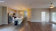 Located in Charlotte, NC, this single-floor home on Landing Place Lane offers a well-designed layout with contemporary finishes throughout. The open-concept living and kitchen area serves as the heart of the home, featuring rich dark hardwood-style flooring, a ceiling fan with warm lighting, and a curved kitchen island with a built-in sink illuminated by elegant pendant lights. The kitchen is equipped with stainless steel appliances — including a refrigerator, electric range, and over-the-range microwave — complemented by light wood cabinetry, white quartz countertops, and a classic subway tile backsplash. Bedrooms are carpeted for comfort and feature ceiling fans and windows with blinds that frame lush, green wooded views, filling each room with natural light. The primary bathroom is a standout space, offering a curved, expansive granite-topped vanity with dual sinks, light wood cabinetry, and wood-style flooring. A secondary bathroom mirrors this refined aesthetic with its own granite vanity, wood-tone cabinetry, and a window overlooking the greenery outside. A dedicated laundry area accommodates a full-size washer and dryer with overhead shelving for additional storage. Neutral tones and clean lines create a cohesive, move-in ready atmosphere throughout.