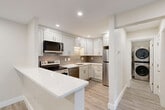 This thoughtfully designed 1-bedroom, 1-bathroom residence in Norwood, MA offers a clean, modern aesthetic throughout its well-utilized single floor. Light gray luxury vinyl plank flooring runs seamlessly through all areas, complemented by recessed lighting and neutral warm-white walls that create a bright, cohesive atmosphere.

The open-concept living, dining, and kitchen area serves as the heart of the home. The kitchen is outfitted with white shaker-style cabinetry, quartz countertops, a taupe subway tile backsplash, and a full suite of stainless steel appliances including a refrigerator, electric range, over-the-range microwave, and dishwasher. A peninsula counter extends the workspace and defines the dining area. The living room benefits from a sliding glass door that invites natural light and provides outdoor access.

The generously sized primary bedroom features recessed lighting and baseboard heating, offering a calm, functional retreat. Three closets throughout the unit — including a spacious walk-in style with built-in shelving and hanging rods — provide ample storage.

The bathroom is finished in a crisp all-white palette with a tub/shower combination, white tile surround, a vanity with storage, and chrome fixtures. A dedicated in-unit laundry area with a stacked washer/dryer adds everyday convenience to this move-in-ready residence.