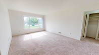 This single-floor unit in the Glenwood community of Dearborn, Michigan presents a well-organized layout designed for comfortable everyday living. The living area is generously proportioned, featuring soft wall-to-wall carpeting and a large sliding window that draws in abundant natural light while offering views of the surrounding greenery. The entry door opens directly into this open space, which flows seamlessly toward the dining area, distinguished by a small chandelier overhead and hardwood-style flooring that marks the transition from the carpeted living space.

The kitchen is laid out in a galley configuration, lined on both sides with dark wood cabinetry providing ample storage. It includes a white electric range with overhead ventilation, a double sink, and hardwood-style flooring underfoot, creating a functional and organized cooking environment.

The bedroom is a comfortable, light-filled room with wall-to-wall carpeting, a window dressed with sheer curtains, and a ceiling light fixture. The neutral walls carry throughout the unit, contributing to a clean, bright ambiance.

The bathroom features white mosaic tile flooring, a full tub and shower combination with white subway-style tile surround, a toilet, and a vanity with cabinet storage — all maintained in a clean, classic style.