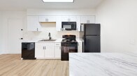 Located at 700 Morreene Rd in Durham, North Carolina, this single-floor residence offers a thoughtfully updated interior with a clean, contemporary aesthetic throughout. The open-concept living and kitchen area serves as the heart of the home, where light wood-look flooring flows seamlessly underfoot and large windows invite abundant natural light from multiple directions. A skylight overhead further brightens the space, enhancing its airy, welcoming atmosphere.

The kitchen is a standout feature, appointed with crisp white shaker-style cabinetry, sleek marble-look countertops, and a matching island peninsula that provides additional workspace and casual dining potential. Black appliances — including a refrigerator, range, microwave, and dishwasher — create a bold contrast against the bright cabinetry, while a modern black-fixtures sink adds a cohesive finishing touch.

The living area transitions naturally into carpeted bedroom spaces, each finished with neutral walls and clean white trim. One bedroom features a built-in closet and a window with blinds, while another offers a convenient built-in shelving unit, providing practical storage solutions. The bathroom is finished in a simple, clean style with light flooring, a white vanity, and modern hardware. Overall, the residence presents a well-maintained, move-in-ready environment with a neutral palette suited to a variety of furnishing styles.