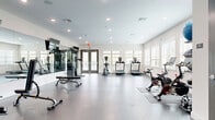 Located at 6568 Halo Bend Ct in Wesley Chapel, FL, this fitness center offers a well-appointed, single-floor exercise space designed to support a comprehensive workout experience. The room features a polished concrete floor that gives the space a clean, modern aesthetic, while recessed lighting and multiple large windows with blinds flood the interior with ample natural light and views of the surrounding outdoors.

The layout is open and generously proportioned, providing plenty of room to move freely between equipment stations. A full-length wall mirror on one side enhances the sense of space and allows users to monitor their form during workouts. Cardio equipment includes treadmills, an elliptical trainer, a stationary upright bike, and a spin bike, all positioned near the windowed walls to take advantage of the natural light. Strength training is supported by a cable machine, a multi-functional weight station, an adjustable bench, and a rack of dumbbells in varying weights.

Stability balls and additional accessories are neatly organized along one wall, adding versatility to the available workout options. Entry is through a set of double glass-panel doors, contributing to an inviting, accessible atmosphere. The clean white walls, neutral tones, and thoughtful equipment arrangement make this fitness center a functional and comfortable space for a wide range of exercise routines.
