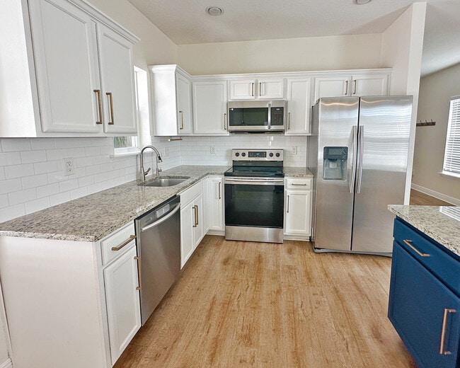 Modern kitchen with white cabinetry, stainless steel appliances, and a large island. - 1736 W Walnut St House
