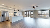 This well-appointed three-bedroom, two-bathroom residence in Cleveland's West Side offers a thoughtfully designed single-floor layout with generous living space. The open-concept kitchen and living area serves as the heart of the home, featuring sleek white cabinetry, a large central island with quartz countertops, stainless steel appliances, and stylish pendant lighting. Wood-look flooring flows throughout the main living areas, while large black-framed windows and sliding glass doors flood the space with natural light and provide access to a private balcony with outdoor views. The spacious primary bedroom is highlighted by oversized windows offering neighborhood views and includes a walk-in closet with wire shelving. Two additional bedrooms feature plush carpeting and ample natural light. Both bathrooms are finished in a clean, modern style — one with a full tub-shower combo, light tile flooring, and dark vanity cabinetry. A dedicated laundry room houses a full-size washer and dryer alongside a dark countertop workspace. Two hallways connect the space efficiently, and a welcoming entrance foyer completes the layout. Neutral gray walls and consistent finishes throughout create a cohesive, contemporary ambiance.