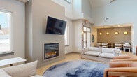 Located at 95 Newport Ave in East Providence, Rhode Island, this thoughtfully designed single-floor community space offers a generous and versatile layout. The welcoming entrance lobby features light hardwood flooring, floor-to-ceiling glass doors that flood the space with natural light, and a built-in bench for comfortable seating. A dedicated mailroom with a marble-topped sorting counter adds practical convenience.

The expansive living room is a standout, boasting dramatically soaring ceilings with clerestory windows that draw in abundant natural light. A modern built-in fireplace anchors the room, complemented by a wall-mounted television, light hardwood floors, and a large area rug. A secondary lounge area with a sectional sofa provides additional relaxed seating.

The kitchen is a design highlight, showcasing a striking blue penny-tile accent wall, sleek gray cabinetry with brass hardware, crisp white quartz countertops, stainless steel appliances, and a central island with bar seating beneath elegant globe pendant lighting. Open shelving adds both style and function.

The two bedrooms, including a generously sized primary bedroom, offer quiet retreats with neutral tones and hardwood flooring. Throughout the space, a cohesive modern aesthetic is maintained through clean lines, soft neutral palettes, and contemporary finishes.