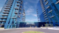 This single-floor space is situated within a striking contemporary building complex characterized by an expansive glass-and-steel exterior facade, offering a sleek and modern architectural presence. The surrounding grounds are well-maintained, featuring landscaped planting beds, open paved areas, and mature trees that contribute to a calm and professional exterior environment.

Inside, the space is designed with a serene, wellness-oriented aesthetic. The primary room features neutral-toned carpeting and clean white walls, creating a calm and uncluttered atmosphere. A standout design element is a large-scale photographic wall mural depicting a classical Buddha sculpture rendered in warm sepia and earth tones, lending the room a contemplative and tranquil character.

Access between areas is provided through two distinct door systems: a frameless glass sliding door partition with frosted panels and stainless steel hardware, offering visual separation while maintaining a sense of openness, and a solid panel barn-style sliding door with brushed stainless steel rail and handles, providing full privacy when needed. Both door systems contribute to the space's refined, minimalist design language. Recessed and linear ceiling lighting provides consistent, even illumination throughout, complementing the overall atmosphere of quiet, purposeful calm.