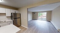 Located at 407 E Seventh St in Monticello, Minnesota, this updated single-floor residence offers a well-designed open layout that seamlessly connects the kitchen and living areas. Light-toned luxury vinyl plank flooring runs throughout, lending a clean and cohesive aesthetic to the entire space.

The kitchen is thoughtfully appointed with white shaker-style cabinetry, light countertops, a classic subway tile backsplash, a double-basin sink with a matte black faucet, stainless steel appliances including a refrigerator and dishwasher, and a peninsula with a built-in cooktop — providing both prep space and a casual dining option.

The spacious living area is filled with natural light and features a sliding glass door that opens to a private balcony, offering pleasant outdoor views. Baseboard heating is present throughout, and a wall-mounted air conditioning unit serves the living space.

The bedroom is generously sized, featuring a ceiling fan, a natural light-filled window, and a dedicated closet. A second room with dual closets provides excellent storage or flexible use as an additional bedroom or office.

The full bathroom is finished with a white vanity, light countertop, matte black hardware, a large mirror, and a tub-shower combination, all set on matching luxury vinyl plank flooring. The space presents a fresh, move-in ready environment.