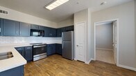 This single-floor unit offers a well-designed layout that balances modern aesthetics with functional living. The kitchen is a standout feature, showcasing bold navy blue shaker-style cabinetry paired with crisp white subway tile backsplash and light quartz countertops. A full suite of stainless steel appliances — including a refrigerator, range with oven, built-in microwave, and dishwasher — provides everything needed for day-to-day cooking. Warm wood-look plank flooring runs throughout the kitchen and living areas, adding a cohesive, contemporary feel. The living and dining areas are open and airy, with large windows fitted with horizontal blinds that invite natural light and neighborhood views. A pass-through opening connects the kitchen to the living space, enhancing the open-concept flow. A double-door closet offers convenient storage near the entryway. The bedroom is generously sized, finished with plush neutral carpeting, a ceiling fan with light fixture, and a window that provides natural light. An additional carpeted room with closet access offers flexible use as a second bedroom or office. The bathroom is clean and modern, featuring wood-look tile flooring, a vanity with quartz countertop, and a full soaking tub with shower combination.