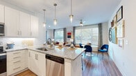 Located at 3250 Buford Hwy in Duluth, Georgia, this single-floor residence offers a thoughtfully designed open-concept layout that seamlessly connects the kitchen, dining, and living areas. The kitchen is outfitted with crisp white shaker cabinetry, granite countertops, a large center island with a stainless steel sink, and a full suite of stainless steel appliances, including a refrigerator, range, microwave, and dishwasher. Elegant pendant lighting and a chevron tile backsplash add refined detail throughout. The open living area is filled with natural light from large windows dressed with patterned drapes and wood blinds, creating a warm and inviting atmosphere. A ceiling fan adds comfort overhead. The adjacent dining area features wood-look flooring and windows overlooking greenery outside. The bedroom is carpeted and generously sized, with large windows that continue the home's bright aesthetic. It connects directly to a spacious walk-in closet with custom built-in shelving and hanging rods. The bathroom is clean and functional, with granite vanity counters, white cabinetry, tile flooring, and a tub-shower combination. Wood-look flooring flows throughout the main living spaces, tying the home's modern, cohesive design together.