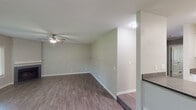 This single-floor residence offers a functional and well-organized layout designed for comfortable everyday living. The open-concept living and dining area features wood-look hard flooring and a subtle raised platform section, adding a distinctive architectural detail to the space. A ceiling fan with light fixture provides both comfort and illumination, while a sliding glass door floods the area with natural light and provides direct access to an outdoor patio with views of surrounding greenery.

The kitchen is defined by a wraparound peninsula counter with a stainless steel sink and modern gooseneck faucet, dark cabinetry, and a suite of black appliances including a refrigerator, range, and over-the-range microwave. A textured ceiling carries throughout the common areas, adding a classic residential character.

The bedrooms are carpeted and finished in neutral tones, each featuring window blinds that allow for natural light and privacy. The rooms offer generous wall space suitable for a variety of furniture arrangements.

Two bathrooms serve the residence. One full bathroom includes a tub-shower combination, a dark-cabinetry vanity with a white countertop sink, and wood-look tile flooring. A second bathroom features a similar vanity setup with a dedicated toilet area, providing added convenience for residents.