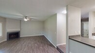 This single-floor residence offers a functional and well-organized layout designed for comfortable everyday living. The open-concept living and dining area features wood-look hard flooring and a subtle raised platform section, adding a distinctive architectural detail to the space. A ceiling fan with light fixture provides both comfort and illumination, while a sliding glass door floods the area with natural light and provides direct access to an outdoor patio with views of surrounding greenery.

The kitchen is defined by a wraparound peninsula counter with a stainless steel sink and modern gooseneck faucet, dark cabinetry, and a suite of black appliances including a refrigerator, range, and over-the-range microwave. A textured ceiling carries throughout the common areas, adding a classic residential character.

The bedrooms are carpeted and finished in neutral tones, each featuring window blinds that allow for natural light and privacy. The rooms offer generous wall space suitable for a variety of furniture arrangements.

Two bathrooms serve the residence. One full bathroom includes a tub-shower combination, a dark-cabinetry vanity with a white countertop sink, and wood-look tile flooring. A second bathroom features a similar vanity setup with a dedicated toilet area, providing added convenience for residents.