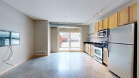 Located at 515 SE Huron Blvd in Minneapolis, Minnesota, this efficiently designed single-floor unit offers a thoughtful open-concept layout that maximizes every square foot. The combined living, dining, and kitchen area forms the heart of the space, anchored by polished concrete floors that lend an industrial-modern aesthetic throughout. Exposed ductwork running along the upper wall adds an urban loft character, while track lighting overhead provides flexible, well-distributed illumination.

The kitchen is well-appointed with light maple cabinetry, dark granite-style countertops, a classic subway tile backsplash, and a full suite of stainless steel appliances including a refrigerator, range, microwave, and dishwasher. Open metal shelving adds both storage and visual interest. A large sliding glass door floods the living area with natural light and opens directly onto a private balcony, offering views of the surrounding neighborhood.

The bathroom features light ceramic tile flooring, a walk-in shower, a toilet, and built-in shelving for storage. A dedicated laundry area houses a stacked full-size washer and dryer unit, adding everyday convenience. The overall ambiance is clean, modern, and functional — well-suited for urban living in the heart of Minneapolis.