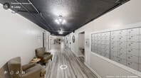Located in the heart of downtown Raleigh, NC, the lobby at 500 E Hargett St offers a well-appointed first-floor common area that combines modern aesthetics with practical amenities. The space is characterized by sleek, light-toned wood-look tile flooring that runs throughout, contrasted by a dark, textured ceiling with exposed ductwork that lends an industrial yet refined atmosphere. Contemporary light fixtures illuminate the corridor, creating a bright and welcoming environment.

The main hallway serves as the central artery of the lobby, lined with resident unit doors and thoughtfully decorated with wall art, ornamental console tables, and potted plants that add warmth and character. A bank of individual resident mailboxes is conveniently situated along the hallway wall, providing easy access for all residents.

Near the entrance, a comfortable lounge area features upholstered seating and a small side table, offering a relaxed spot to unwind. A bookshelf stocked with reading materials and a wall-mounted TV provide additional leisure options. The glass-panel entry doors allow natural light to filter into the space, connecting the interior to the outdoors.

Completing the lobby is a dedicated exercise room, ensuring residents have convenient access to fitness facilities. The overall design strikes a balance between urban industrial style and residential comfort, making this lobby a functional and inviting gateway to the building.