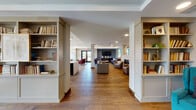 Located at 31 E Ogden Ave in La Grange, IL, this thoughtfully designed single-floor community space combines contemporary architecture with warm, inviting interiors. Wide-plank hardwood flooring flows throughout, anchoring an open-concept layout that seamlessly connects multiple distinct lounge and gathering areas.

The main common area is framed by built-in bookshelves flanking structural columns, creating a welcoming library-style entrance that opens into a spacious lounge with multiple seating arrangements. A wall-mounted television with a dark accent surround serves as a focal point, complemented by a fireplace and tray ceilings with recessed and ambient lighting that add architectural depth.

Several distinct seating vignettes offer flexible gathering options, including a leather sofa lounge with floor-to-ceiling windows that invite abundant natural light and outdoor views. Warm-toned furnishings, including leather sofas, accent chairs, and a round marble coffee table, create a comfortable yet polished atmosphere.

A formal private dining room features a solid wood conference-style table, upholstered seating, decorative geometric wallcovering, and a linear pendant light fixture overhead. The chef-quality kitchen is a standout, showcasing a large marble waterfall island with bar seating, navy cabinetry, a professional-grade range with stainless hood, textured tile backsplash, and pendant lighting — ideal for community events and gatherings.