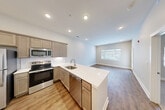 Located at 6276 Newton Rd in Haslett, Michigan, this thoughtfully designed one-bedroom, one-bathroom unit offers a clean, modern aesthetic throughout its efficiently organized single-floor layout. The open-concept kitchen and living area serves as the heart of the home, featuring warm taupe cabinetry, a classic subway tile backsplash, and a full suite of stainless steel appliances including an electric range, built-in microwave, and dishwasher. A generous peninsula with a sleek white quartz countertop provides additional prep space and casual seating, flowing seamlessly into the bright living area. Wood-look plank flooring runs throughout the main living spaces, complemented by recessed lighting and a neutral color palette that creates a cohesive, contemporary feel. A glass-panel door opens to an outdoor balcony area, bringing in natural light and a connection to the exterior. The bedroom offers plush carpeting, natural light through a window with blinds, and comfortable proportions. The full bathroom includes a white vanity with countertop, wood-look flooring, and direct access to the adjacent bedroom. A dedicated closet and a separate in-unit laundry space with a stacked washer and dryer round out the practical amenities of this well-appointed home.