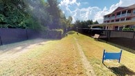 Located at 980 Courthouse Rd, this single-story property features a notable outdoor area that serves as a key characteristic of the space. The exterior yard is enclosed by a dark privacy fence, providing clear boundaries and a sense of seclusion from the surrounding area. The lawn stretches across a generous open expanse, with grass covering the majority of the ground and a worn pathway visible along the center, suggesting regular use of the space.

Mature trees and dense hedgerow line the perimeter, offering natural shade and additional privacy screening. The landscaping creates a layered green backdrop that enhances the outdoor atmosphere. A wooden bench is positioned along the fenced edge, providing a designated seating area and adding a functional, welcoming element to the yard.

The terrain features a gentle slope toward the far end of the yard, adding subtle topographic interest to the space. Natural light fills the area openly, benefiting from an unobstructed sky above. The overall character of the outdoor space is practical and well-defined, suited for a variety of uses while maintaining a calm, green setting.