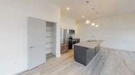 Located at 255 N Goodman St in Rochester's vibrant East End neighborhood, this single-floor residence showcases a clean, contemporary design throughout. Light-toned hardwood flooring flows seamlessly across the open-concept living and kitchen areas, creating a cohesive and airy atmosphere.

The kitchen is a standout feature, centered around a substantial island with an undermount sink and quartz-style countertops. Dark wood cabinetry on the lower level contrasts sharply with crisp white upper cabinets, while stainless steel appliances—including a refrigerator, range, and built-in microwave—add a polished finish. A textured tile backsplash and pendant lighting over the island complete the space. A walk-in pantry provides generous storage. Large black-framed windows flood the living area with natural light and frame elevated views of the surrounding Rochester streetscape.

The bedrooms are generously proportioned, each featuring oversized black-framed windows offering urban views, light hardwood floors, and closet space. The bathroom presents a clean, minimalist aesthetic with tile flooring, a dark wood vanity with quartz countertop, a glass-enclosed shower, and chrome fixtures throughout.