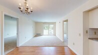 Located at 600 Bennett Way in Newmarket, NH, this single-floor, three-bedroom, two-bathroom home offers a practical and comfortable layout. The living room is a welcoming space featuring warm hardwood-style flooring at the entry, soft carpeting throughout, and an elegant chandelier overhead. Sliding glass doors open to an outdoor balcony, flooding the room with natural light and providing pleasant views of the surrounding greenery. The kitchen is efficiently designed with white cabinetry, granite-style countertops, a classic subway tile backsplash, and hardwood flooring — providing a clean, functional workspace. The primary bedroom is generously sized, featuring a walk-in closet with wire shelving, offering ample storage. The additional bedrooms are carpeted and bright, each with built-in closets and windows that invite natural light. The two bathrooms feature hardwood-style flooring and clean, simple finishes. A hallway connects the living areas to the bedrooms, creating a logical and efficient flow throughout the home. Overall, the space presents a neutral, move-in-ready aesthetic with light-toned walls, consistent flooring materials, and a cohesive design that balances functionality with everyday comfort.
