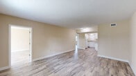 This single-floor unit offers a clean, updated interior finished with light wood-look flooring that runs consistently throughout the space, creating a cohesive and modern aesthetic. The open living area is generously proportioned, featuring warm beige walls, white baseboards, and a textured ceiling. Large windows allow natural light to fill the room while providing views of surrounding greenery, enhancing the bright and airy atmosphere.

The kitchen is thoughtfully appointed with white shaker-style cabinetry, granite-look countertops, and a full suite of white appliances including a coil-top range with overhead ventilation. A pass-through opening connects the kitchen to the living and dining areas, promoting an open flow ideal for everyday living.

The bedrooms are well-sized and well-lit, each with access to closet space. The bathrooms feature updated white vanities with granite countertops, undermount sinks, large mirrors, and wire shelving for added storage. Wood-look tile flooring carries through these spaces, maintaining visual consistency.

The floor plan, as shown in the dollhouse view, reflects a practical and functional layout with clear separation between living, sleeping, and utility areas. Overall, this space presents a freshly updated interior with neutral finishes suited to a variety of furnishing styles.