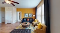 Located at 14650 Foliage Ave in Apple Valley, Minnesota, this single-floor residence offers a thoughtfully designed layout with a cohesive contemporary aesthetic throughout. The living room makes a strong first impression with a bold amber accent wall, rich hardwood-style flooring, and large windows dressed in floor-to-ceiling dark drapes that allow generous natural light to fill the space. A ceiling fan, comfortable seating arrangement, and a round wooden coffee table anchored by a geometric area rug complete the welcoming atmosphere. The front entry features a transom window above the door, adding additional light to the space. The kitchen is well-appointed with dark espresso cabinetry, granite-style countertops, black appliances, and a built-in wine rack. A peninsula island with bar seating and pendant lighting overhead makes it ideal for casual dining and entertaining. Hardwood-style flooring continues seamlessly from the living area into the kitchen. The bedrooms offer plush carpeting, ceiling fans, and windows with blinds and curtain panels. One bedroom features a vibrant yellow accent wall, while another presents a more neutral, serene palette. Both provide comfortable, restful environments. The bathroom includes a full tub-shower combination, dark vanity with granite-style countertop, and hardwood-style flooring, rounding out this well-maintained and stylishly appointed home.