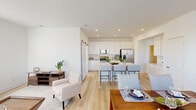 This two-story home presents a clean, contemporary design characterized by crisp white walls, light wood-look flooring, and an abundance of natural light throughout. The main floor showcases an open-concept layout where the kitchen, dining, and living areas flow seamlessly together. The kitchen is outfitted with white shaker cabinetry, stainless steel appliances including a French door refrigerator and built-in microwave, light quartz countertops, and a central island with bar seating. A sliding barn door adds a stylish accent nearby. The dining area accommodates a full-sized table and connects naturally to a comfortable living room, where large windows flood the space with daylight. A dedicated office or flex room features sliding glass doors that open to outdoor views, enhancing its bright and functional character. An entry corridor leads to the staircase, guiding residents to the upper level. Upstairs, the bedrooms are finished with plush carpet and feature ample natural light. One bedroom includes a walk-in closet, while another is well-suited as a children's room. Bathrooms are finished in neutral tones with modern chrome fixtures. Throughout, the home maintains a cohesive, airy aesthetic.