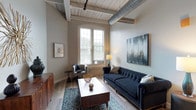 This thoughtfully designed 1-bedroom, 2-bathroom unit with a den showcases a compelling fusion of historic industrial character and contemporary living. The living area makes an immediate impression with its striking soaring ceilings adorned with whitewashed wood planks, exposed structural beams, and bold exposed ductwork — all hallmarks of loft-style design. Large arched windows flood the space with natural light and frame views of the surrounding greenery, while durable hardwood-style flooring runs throughout the main living areas.

The kitchen is outfitted with crisp white shaker cabinetry, stainless steel appliances, and a clean countertop workspace, offering both style and functionality. The bedroom continues the industrial-chic aesthetic with the same distinctive ceiling detail, plush carpeting for comfort, an arched window, and a spacious walk-in closet with built-in wire shelving for generous storage. Both bathrooms are finished in a clean, modern palette with white vanities and light countertops. An in-unit laundry room houses a full-size stacked washer and dryer alongside a water heater, adding everyday convenience. The versatile den provides additional flexible living or workspace, rounding out this well-appointed urban residence.