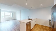 Located at 955 Eleventh Avenue in San Diego, CA, this modern 2-bedroom, 1-bathroom residence offers a thoughtfully designed open-concept layout across a single floor. Light hardwood flooring flows throughout, lending warmth and continuity to each space.

The kitchen and living area form the heart of the home, anchored by a sleek peninsula featuring quartz countertops, an undermount sink, and a stainless steel dishwasher. The kitchen is outfitted with flat-front white cabinetry extending to the ceiling, stainless steel appliances including a French door refrigerator with ice dispenser, a microwave, and a range with tile backsplash — a clean, contemporary aesthetic throughout.

Both bedrooms are bright and airy, benefiting from large floor-to-ceiling windows that frame outdoor views and allow generous natural light to fill the rooms. The spacious primary bedroom offers ample room to furnish comfortably, while the second bedroom provides flexibility for guests or a home office.

The bathroom is finished with elegant marble-style tile surrounding a full soaking tub and shower, complemented by a floating white vanity with a warm-toned countertop and a large frameless mirror. In-unit laundry is also conveniently accessible. Recessed lighting and crisp white walls complete this modern, move-in-ready residence.