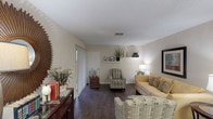 This single-story, one-bedroom, one-bathroom residence offers a thoughtfully organized layout that maximizes its available square footage. The living room serves as the central gathering space, featuring rich dark hardwood-style flooring, neutral beige walls, and a built-in display shelf ideal for décor and personal items. A sliding glass door allows natural light to filter into the room, creating a bright and welcoming atmosphere. The open sightlines from the living area connect visually to the dining space, enhancing the sense of openness.

The kitchen is efficiently designed with white cabinetry, light-toned countertops, and white appliances including an electric range and over-the-range microwave. A pass-through view into the dining area promotes easy interaction between spaces.

The bedroom is carpeted and comfortably sized, equipped with a ceiling fan with light fixture and windows fitted with blinds and drape panels for light control. The full bathroom includes a tub-shower combination, a vanity with countertop space, and a mirror with overhead lighting. Overall, the residence presents a clean, neutral palette with functional finishes throughout.