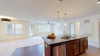 Located at 1001 Aventine Dr in Arden, NC, this well-appointed three-bedroom, two-bathroom single-floor residence offers a thoughtfully designed layout across a generously sized floor plan. The open-concept kitchen and living area serves as the heart of the home, featuring rich dark-wood cabinetry, dark granite countertops, a tile backsplash, and a full suite of stainless steel appliances including a refrigerator, range, and microwave. A large kitchen island with an undermount sink and pendant lighting anchors the space, flowing seamlessly into the living room, which is brightened by natural light from multiple windows with blinds and accented by a ceiling fan. Hardwood-style flooring runs throughout the main living and kitchen areas, while plush neutral carpet extends into all three bedrooms. Each bedroom is equipped with a ceiling fan and windows overlooking lush greenery, creating a calm and airy atmosphere. The spacious primary bedroom includes its own walk-in closet with wire shelving. A total of six closets throughout the home provides exceptional storage capacity. The primary bathroom features a glass-enclosed walk-in shower, wood-toned vanity, and hardwood-style flooring. A dedicated laundry area and a connecting hallway complete this functional and comfortable single-level home.