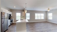 This single-floor residence offers a thoughtfully designed open-concept layout that seamlessly connects the kitchen and living area. The kitchen is outfitted with white shaker-style cabinetry, quartz countertops, a dark subway tile backsplash, stainless steel appliances, and a peninsula with an integrated sink and pendant lighting overhead. The adjoining living area is generously proportioned, featuring warm wood-look flooring, a ceiling fan, and multiple windows that invite abundant natural light and outdoor views.

A hallway with a louvered utility closet leads to the private quarters of the home. The bedrooms are carpeted for comfort and each feature ceiling fans and windows with views of the surrounding landscape. The primary bedroom includes a walk-in closet equipped with wire shelving and rack systems, providing ample storage.

Both bathrooms are finished consistently, each offering a quartz-topped vanity with white cabinetry, tile flooring, and a full tub-shower combination with floor-to-ceiling tile surround and a curved curtain rod. The neutral warm-gray color palette carried throughout the home creates a cohesive and calming ambiance. Clean lines, consistent finishes, and an abundance of natural light define the overall character of this well-appointed residence.
