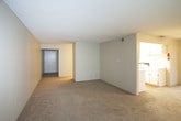 This single-floor unit offers a practical and straightforward layout across several well-defined spaces. The living area is generously sized, featuring wall-to-wall carpet in a neutral tone and a ceiling fan with light fixture overhead. A window fitted with horizontal blinds allows natural light to filter in, creating a comfortable atmosphere. An adjacent sliding glass door provides access to the outdoors, where lush greenery is visible, enhancing the sense of connection to the surrounding environment.

The galley-style kitchen is efficiently designed with white cabinetry lining both sides, light-toned countertops, a double-basin sink, and white appliances including an electric range, dishwasher, and refrigerator. Wood-style flooring runs the length of the kitchen, providing a clean contrast to the carpeted living areas. The kitchen opens toward a hallway that connects to the remainder of the unit.

The bedroom spaces are carpeted and well-proportioned, each featuring windows with views of surrounding greenery. At least one bedroom includes a reach-in closet with bifold doors and a rod for hanging storage. The bathroom is outfitted with tile flooring, a tub and shower combination with white tile surround, a toilet, and a vanity with sink. Chrome towel bars and a textured ceiling complete the functional space.