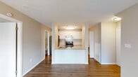 This single-floor residence offers a clean, functional layout designed for comfortable everyday living. Warm wood-look flooring flows consistently throughout the space, tying each room together with a cohesive aesthetic. Neutral beige tones on the walls complement the bright white trim and baseboards, creating an inviting and versatile atmosphere.

The kitchen serves as a central hub, featuring a peninsula with light stone-look countertops that opens to the main living area. White shaker-style cabinetry lines the walls, providing ample storage, while a textured geometric tile backsplash adds visual interest. Stainless steel appliances—including a refrigerator, electric range with overhead vent hood, and sink—complete the functional cooking space.

The living area is generously sized, illuminated by a ceiling fan with integrated lighting and access to an outdoor area via vertical blinds. A textured ceiling adds subtle character throughout the common areas. The bedroom features a window dressed with blinds, allowing natural light to filter in while maintaining privacy.

The bathroom is well-equipped with a soaking tub, a separate vanity area with stone-top cabinetry, a vessel sink, and a large mirror. A bifold closet door provides convenient storage access. An additional bathroom is visible nearby, offering a second vanity and window. The layout is practical and efficiently organized for single-level living.