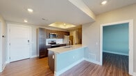 Located at 114 E. 5th Street in Columbus, Ohio, this single-floor unit offers a thoughtfully designed open-concept layout with contemporary finishes throughout. The kitchen serves as a central hub, showcasing rich dark-stained cabinetry, quartz countertops, a peninsula with an undermount sink, and a full suite of stainless steel appliances including a refrigerator, electric range, microwave, and dishwasher. A dedicated utility closet provides additional convenience. The kitchen flows seamlessly into the living area, which features hardwood-style plank flooring and a neutral color palette that enhances the sense of openness. A glass-paneled door leads to a private balcony, allowing natural light to pour into the space and offering pleasant outdoor views. The bedroom is carpeted for comfort, features a window with natural light, and connects directly to the main living area through a paneled interior door. The bathroom is well-appointed with wood-look flooring, dark vanity cabinetry, a white quartz countertop, and a frameless glass-enclosed walk-in shower with marble-style tile surround. Recessed lighting, clean white trim, and consistent neutral tones throughout the unit contribute to a polished, modern aesthetic ideal for everyday living.