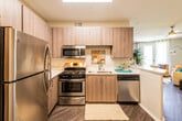 This single-floor residence offers a thoughtfully designed layout that balances modern aesthetics with practical functionality. The kitchen is a standout feature, equipped with a full suite of stainless steel appliances including a gas range, over-the-range microwave, dishwasher, and refrigerator. Warm-toned wood-grain cabinetry extends to the ceiling, providing ample storage, while white countertops offer a clean contrast. A dedicated entryway with hardwood-style flooring leads seamlessly into the kitchen and living areas, creating a welcoming first impression. The open living room is bright and inviting, featuring dark hardwood-style floors, a ceiling fan with integrated lighting, large windows with sheer white curtains, and a glass door that opens to an outdoor area, allowing natural light to fill the space. The bedroom is a calm, carpeted retreat with a ceiling fan, soft neutral-toned walls, and tasteful décor. The full bathroom includes a soaking tub with shower, wood-grain vanity cabinetry, and hardwood-style flooring, maintaining the cohesive design language found throughout the residence. Overall, the space presents a contemporary and comfortable living environment with consistent, modern finishes.