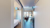 This two-floor residence showcases a contemporary urban design with industrial-inspired elements seamlessly integrated throughout. The main living area features soaring ceilings with exposed ductwork and large sliding glass doors that open to a balcony, flooding the space with natural light and offering expansive city views. Hardwood-style flooring runs throughout the main level, complementing the open-concept layout that connects the living, dining, and kitchen areas.

The kitchen is well-appointed with granite countertops and backsplash, dark lower cabinetry paired with white upper cabinets featuring frosted glass inserts, stainless steel appliances, and a built-in wine rack. A breakfast bar provides additional seating.

The primary bedroom is accessed via frosted glass sliding panel doors and features clerestory windows that draw in additional light, along with a built-in closet. A second bedroom on the lower level offers carpeted flooring, a ceiling fan, and a dedicated desk area. Both bedrooms are served by their own bathrooms — one with a glass-enclosed walk-in shower and a floating vanity, and the other with a shower-tub combination and adjacent built-in shelving. A walk-in closet with wire shelving provides ample storage.