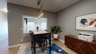 This thoughtfully designed single-floor workspace blends functionality with contemporary aesthetics throughout its distinct zones. The flooring is a standout feature, with light-toned herringbone-patterned wood running seamlessly across the space, lending warmth and visual interest underfoot.

The meeting or conference area serves as a central gathering point, anchored by a substantial wood-top bar-height table surrounded by upholstered charcoal chairs. A striking multi-pendant chandelier with gold and black accents descends overhead, while a frosted glass interior window connects visually to the adjacent area. A vibrant blue abstract area rug and a lush tropical plant add color and life to the room. A walnut-finished credenza with geometric gold inlay detailing provides additional storage.

The workstation nook is designed for focused productivity, featuring a built-in white floating desk that wraps around a dividing column, accommodating multiple monitors. Warm globe pendant lighting and a boldly patterned geometric accent wall in soft gold tones create an energizing yet comfortable environment for individual work.

The kitchenette is sleek and fully equipped, showcasing navy cabinetry with fluted glass upper doors and gold hardware, a stainless steel sink, microwave, coffee station, and additional appliances. Together, these spaces form a cohesive, modern professional environment with strong attention to design detail.