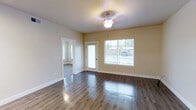 This single-floor space offers a clean, open-concept design that seamlessly connects the living and kitchen areas, creating a spacious and functional layout. The living area features rich, dark hardwood-style flooring that contrasts beautifully with the light-toned walls, lending warmth and a polished finish to the space. A ceiling fan with a light fixture provides both comfort and illumination, while large windows fitted with white blinds invite generous natural light and offer views of the outdoor surroundings. A door provides convenient exterior access directly from the living area.

The kitchen is thoughtfully designed with white shaker-style cabinetry, light stone-look countertops, and a peninsula that serves as both a workspace and casual dining option. Stainless steel appliances, including a refrigerator and microwave, complement the modern aesthetic, while track lighting above ensures the kitchen is well-lit. The kitchen's bright, neutral palette pairs harmoniously with the adjoining living space, reinforcing the open and airy ambiance found throughout. Overall, the space presents a fresh, move-in-ready environment with cohesive design choices and practical features throughout.