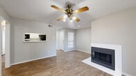 This thoughtfully designed 2-bedroom, 2-bathroom residence offers a practical and comfortable single-floor layout. The living room serves as the centerpiece of the home, featuring a striking white-surround corner fireplace with a sleek black firebox, warm hardwood-style flooring, and a ceiling fan with light fixture. Natural light enters through a large sliding glass door fitted with vertical blinds, providing access to an outdoor area. A pass-through opening connects the living space to the kitchen, which includes white cabinetry and appliances. Both bedrooms are finished with the same hardwood-style flooring and neutral wall tones. The primary bedroom includes a walk-in closet with built-in shelving and hanging rods, as well as its own ceiling light fixture. The second bedroom also features a spacious closet with organized shelving. Each bathroom is appointed with a full tub-shower combination surrounded by clean white tile, a vanity with storage, and matching flooring. A connecting hallway with additional closet storage ties the layout together efficiently. Textured ceilings are consistent throughout, and the overall neutral color palette creates a bright, clean atmosphere across the entire residence.