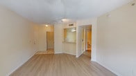 This single-floor unit offers a clean, functional layout with a bright and airy atmosphere throughout. The open living area is finished with light wood-style flooring and neutral beige walls, creating a warm and welcoming ambiance. A textured ceiling with a ceiling fan adds character, while large windows and a glass-panel door flood the space with natural light and provide views of the surrounding outdoor greenery.

The kitchen is efficiently designed with light wood cabinetry, light-toned countertops, and tile flooring. It is equipped with a full suite of white appliances, including an electric range with a smooth cooktop, a dishwasher, a full-size refrigerator, and a microwave. A pass-through opening connects the kitchen to the main living area, enhancing the open feel of the space.

The bedroom is a comfortable, well-proportioned room featuring the same light wood-style flooring, a ceiling fan with a light fixture, and a window that lets in ample natural light with views of the outdoors.

The bathroom is neatly appointed with tile flooring, a single-sink vanity with light wood cabinetry, a large mirror, and a full bathtub with a shower surround. The entry area features tile flooring and provides access to the main living spaces. Overall, the unit presents a practical and well-maintained living environment.