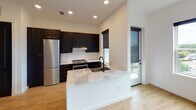 Located at 4331 Barclay Downs Dr in Charlotte, NC, this modern single-floor residence combines contemporary design with high-quality finishes throughout. The open-concept layout centers around a well-appointed kitchen that serves as the heart of the home, showcasing bold dark shaker-style cabinetry with gold hardware, striking marble-look quartz countertops, a classic white subway tile backsplash, and a full suite of stainless steel appliances including a built-in refrigerator and electric range. A large kitchen island with an integrated sink and waterfall countertop provides additional workspace and casual dining opportunities, with a glass door nearby offering access to an outdoor area and filling the space with natural light. Light-toned hardwood flooring runs seamlessly throughout the living areas, complementing the crisp white walls and creating a bright, airy atmosphere. The bedroom is well-proportioned and benefits from natural light through a window with exterior views, and is equipped with a ceiling fan for year-round comfort. The bathroom is finished with large-format porcelain tile, a soaking tub with full tile surround, matte black fixtures, and a dark vanity with white countertop — maintaining the cohesive modern aesthetic found throughout the entire unit.