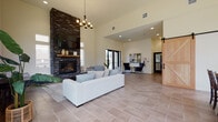 Located at 14014 NE Salmon Creek Ave in Vancouver, Washington, this single-story clubhouse facility presents a thoughtfully designed communal space that blends contemporary style with inviting comfort. The interior is anchored by a floor-to-ceiling stacked-stone fireplace, which serves as a commanding architectural focal point in the main lounge. Soaring ceilings amplify the sense of openness, while large black-framed windows and glass double-entry doors flood the space with natural light and provide views of the surrounding community.

The main lounge features large-format tile flooring throughout and is furnished with generous seating arrangements, including a substantial white sofa, patterned accent chairs, and a plaid settee grouped around the fireplace. A chandelier adds a warm finishing touch overhead. A dedicated seating nook near the entrance offers a quieter retreat, outfitted with a pair of sleek black wingback chairs, a checkerboard game table, and an oversized abstract canvas painting. Adjacent to the lounge, a kitchenette area includes a stainless steel refrigerator and a central island with bar seating, all bathed in natural light from an expansive window wall. A sliding barn door adds a rustic-modern accent to the overall design.
