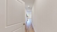 This well-designed two-story home offers a thoughtful layout across two floors, combining modern finishes with functional living spaces. The ground floor features an open-concept kitchen and living area, where light wood-look flooring flows seamlessly throughout. The kitchen is a standout, equipped with stainless steel appliances, a central island with a sink and pendant lighting, a mix of white and warm-toned cabinetry, and open shelving for added character. The living area is bright and airy, with large windows and a glass-paned door that invite abundant natural light and provide views of the outdoors. A hallway with recessed lighting and clean white walls leads to additional spaces, including an attached garage with an automatic door opener. Upstairs, the more expansive floor houses both bedrooms, each featuring plush carpeting, ceiling fans, and multiple windows that frame green outdoor views. The generously sized primary bedroom includes a walk-in closet outfitted with built-in shelving and double hanging rods. The two bathrooms are finished with neutral tile flooring, white cabinetry, quartz-style countertops, and a tiled soaking tub. Throughout the home, a consistent palette of whites and warm neutrals creates a clean, contemporary ambiance.