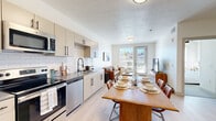 Located at 105 E Turner Mill Rd in Heber City, Utah, this thoughtfully designed single-floor residence offers a clean, contemporary aesthetic throughout. The open-concept layout seamlessly connects the kitchen, dining, and living areas, creating a bright and functional space filled with natural light from large windows and a glass exterior door. The kitchen is well-appointed with stainless steel appliances including a range, dishwasher, microwave, and refrigerator, complemented by taupe cabinetry with black hardware, a white subway tile backsplash, and dark countertops. A substantial wood dining table anchors the dining area, which flows naturally into the inviting living room featuring direct outdoor access. The bedrooms are serene and well-lit, each with ample natural light from exterior windows. The full bathroom is finished with light cabinetry, a gray countertop vanity, matte black fixtures, and a combination tub and shower. Light wood-style flooring runs throughout the main living areas, while the bedrooms feature neutral carpeting. A practical mudroom entry with built-in bench seating, coat hooks, and shelving adds everyday convenience. The hallway connects all rooms with ease, lending the floor plan a cohesive, organized flow suited for comfortable living in the heart of Heber City.