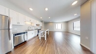 This well-designed single-floor residence offers a thoughtfully laid-out open-concept living space that seamlessly connects the kitchen, dining, and living areas. The kitchen is a standout feature, boasting crisp white shaker cabinetry extending to the ceiling, granite countertops, a full suite of stainless steel appliances including a refrigerator, dishwasher, and range, and a center island with a granite top that doubles as a casual dining surface. Recessed lighting and a tile backsplash complete the polished look. Rich hardwood-style flooring flows throughout the main living areas, while plush carpet adds comfort to the bedrooms. Multiple bedrooms are present, each offering generous proportions and natural light from large windows. The primary bedroom includes a spacious walk-in closet with built-in wire shelving and an en-suite bathroom featuring a granite-topped vanity with white cabinetry and a tub-shower combination. A second full bathroom mirrors the same quality finishes. A dedicated in-unit laundry room houses a full-size front-loading washer and dryer. Throughout the residence, neutral gray tones, clean white trim, and consistent finishes create a cohesive, modern aesthetic.