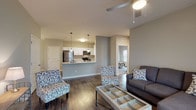 This single-floor villa at Villas of Jeffersonville offers a thoughtfully designed open-concept layout with consistent, modern finishes throughout. The living area features rich hardwood-style flooring, a ceiling fan, and large windows with blinds that allow generous natural light. A sectional sofa and glass-top coffee table anchor the comfortable sitting space, which flows directly into the dining area, complete with a pendant light fixture and room for a full dining set.

The kitchen is well-equipped with white shaker-style cabinetry, light granite countertops, and a full suite of stainless steel appliances including a refrigerator, electric range, microwave, and dishwasher. A peninsula counter provides additional workspace and casual seating.

The unit includes multiple bedrooms, each carpeted and fitted with ceiling fans and windows that bring in natural light. The bedrooms offer closet space and a calm, neutral color palette. The bathroom features a white vanity with granite countertops, a large mirror with an illuminated fixture above, and a full tub-shower combination, all set on hardwood-style flooring. Neutral gray tones are carried throughout the home, creating a cohesive and inviting atmosphere well-suited for comfortable everyday living.